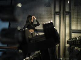 menina morena fitness em roupa esportiva preta em pé perto da prateleira com halteres na academia contra o espelho foto