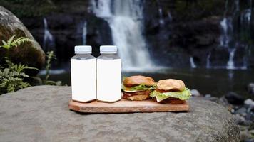 dois hambúrgueres e duas garrafas de bebida na beira da cachoeira foto