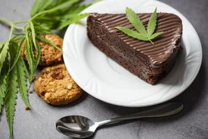Bolo de chocolate e biscoitos com folha de cannabis - planta de folhas de maconha na chapa branca sobre a mesa de madeira, conceito de erva de natureza alimentar de cannabis foto