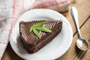 Bolo de chocolate com folha de maconha - planta de folhas de maconha em um prato branco sobre a mesa de madeira, conceito de erva de natureza alimentar de cannabis foto