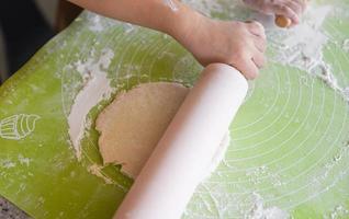 mãos amassam a massa de pastelaria caseira para pão ou pizza de fundo de padaria - mãos de criança preparam a massa e o rolo de massa com farinha a bordo foto