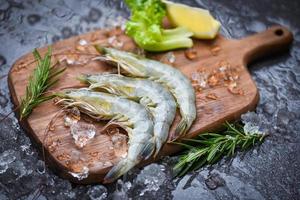 camarão fresco em uma tábua de madeira com ervas ingredientes de alecrim e temperos para cozinhar frutos do mar - camarões crus camarões no gelo congelados no restaurante de frutos do mar