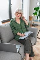 empresário sênior mulher amigável trabalhar em casa. falando ao telefone trabalhar com lap top. negócios, autônoma, conceito de mulher idosa foto