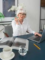 cansado sênior linda mulher de cabelo grisalho na blusa branca, lendo documentos no escritório. trabalho, pessoas seniores, problemas, encontrar uma solução, conceito de experiência foto