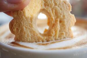 Derramando biscoitos doces em uma caneca de café na mesa de madeira foto