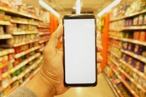 mão segurando Móvel telefone com branco tela enquanto compras às supermercado. foto