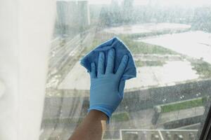 close-up da mão da pessoa em luvas limpando o vidro da janela foto