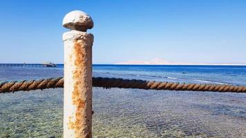 pontão longo no Mar Vermelho no Egito. pontão para descida na água. ponte de madeira no território do hotel amway em sharm el sheikh com cercas de metal e uma corda sobre o mar com ondas foto