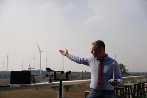 uma Senior masculino energia especialista é inspecionando vento turbinas em a ecológico construção projeto usando uma vento Rapidez medindo instrumento às uma moinho de vento. foto