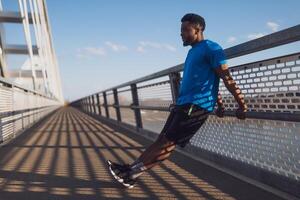 jovem afro-americano homem é exercício em a ponte dentro a cidade. ele é fazendo marcha ré flexões. foto