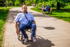 retrato do homem dentro cadeira de rodas. ele é desfrutando ensolarado dia dentro cidade parque. foto
