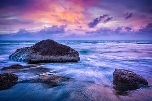 ondas e pedras na praia do pôr do sol foto