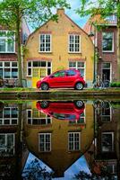 vermelho carro em canal aterro dentro rua do delft. Delft, Países Baixos foto