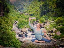 sorte em forma mulher fazendo ioga asana ao ar livre às tropical cascata foto