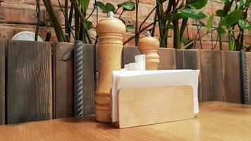 uma mesa em um café ou restaurante. guardanapos brancos em um suporte de madeira, sal e pimenta em uma mesa de madeira. pizzaria com temperos, guardanapos e palitos foto