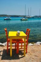 cafeteria mesa de praia dentro Adamantas Cidade em milos ilha com egeu mar com barcos dentro fundo foto