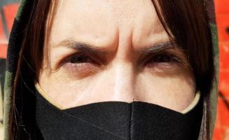 retrato de uma mulher com uma máscara protetora preta ao ar livre perto de uma velha parede quebrada. coronavírus e conceito de poluição do ar. uma garota usa uma máscara protetora para se proteger contra uma pandemia. foto