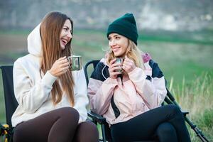 dois jovem mulheres caminhada dentro a montanhas e bebendo chá a partir de uma chaleira. viagem, viajante. foto