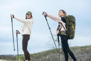 dois jovem mulheres caminhada dentro a montanhas e bebendo chá a partir de uma chaleira. viagem, viajante. foto