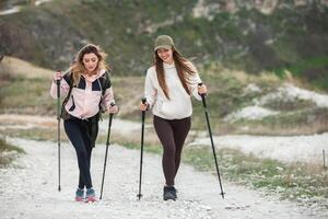 dois jovem mulheres caminhada dentro a montanhas e bebendo chá a partir de uma chaleira. viagem, viajante. foto