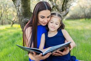 mãe e filha estão lendo juntos dentro a parque foto