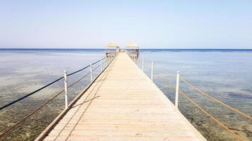 pontão longo no Mar Vermelho no Egito. pontão para descida na água. ponte de madeira no território do hotel amway em sharm el sheikh com cercas de metal e uma corda sobre o mar com ondas foto