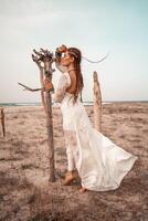 modelo dentro boho estilo dentro uma branco grandes vestir e prata joalheria em a de praia. dela cabelo é trançado, e lá estão muitos pulseiras em dela braços. foto