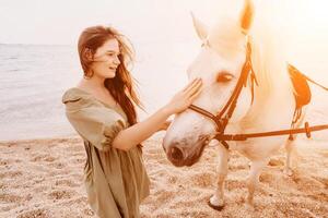 uma mulher dentro uma vestir carrinhos Próximo para uma branco cavalo em uma praia, com a azul céu e mar dentro a fundo. foto