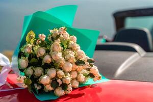 uma ramalhete do flores é sentado em a de capuz do uma vermelho carro. a flores estão branco e vermelho, e elas estão arranjado dentro uma vaso. conceito do romance e amar. foto