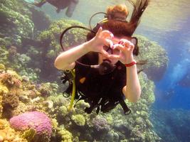 adorável menina mergulhadora mostra com um gesto de mão um sinal de amor, um coração de dedos com um instrutor parceiro para nadar com segurança sob a água no mar vermelho com recifes de coral egito, sharm el sheikh foto