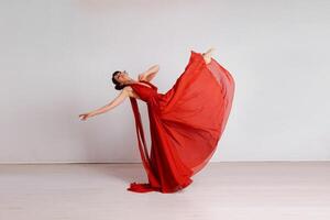 dançarino dentro uma vermelho vôo vestir. mulher bailarina dançando em uma branco estúdio fundo foto