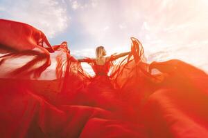 mulher vermelho vôo vestir. uma Loiras dentro uma vermelho vestir contra a céu. traseiro Visão do uma lindo Loiras mulher dentro uma vermelho vestir tremulando dentro a vento contra uma azul céu e nuvens. foto