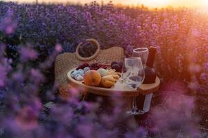 uma piquenique cesta preenchidas com fruta e vinho é conjunto Fora dentro uma campo do roxa flores a cena é sereno e pacífico. foto