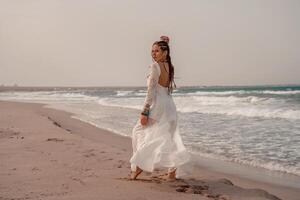 modelo dentro boho estilo dentro uma branco grandes vestir e prata joalheria em a de praia. dela cabelo é trançado, e lá estão muitos pulseiras em dela braços. foto