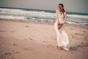 modelo dentro boho estilo dentro uma branco grandes vestir e prata joalheria em a de praia. dela cabelo é trançado, e lá estão muitos pulseiras em dela braços. foto