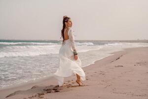 modelo dentro boho estilo dentro uma branco grandes vestir e prata joalheria em a de praia. dela cabelo é trançado, e lá estão muitos pulseiras em dela braços. foto