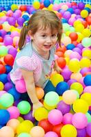 criança feliz jogando nas bolas coloridas foto