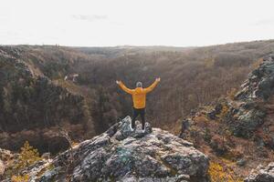 viajante dentro uma amarelo Jaqueta em pé em a Beira do uma Rocha desfrutando uma momento do relaxamento e uma Visão do a divocar sarcástico vale, Praga, tcheco república. alcançar sucesso foto