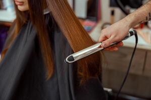 fechar-se do cabeleireiro mão segurando cabelo alisador e fazer Penteado para fêmea cliente foto