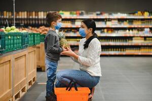 mãe e filho estão compras às a mercearia loja. elas vestem máscaras durante quarentena. coronavírus pandemia .coved-19 clarão. a epidemia do a vírus. foto