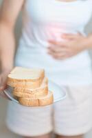 glúten intolerância, glúten livre e celíaco doença ou trigo alergia conceito. mulher aguarde pão e tendo abdominal dor depois de comer glúten. estômago dor, náusea, inchaço, gás, diarréia e pele erupção cutânea foto