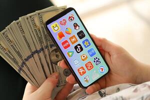 Kyiv, Ucrânia - abril 1, 2024 ásia apps ícone em Smartphone tela e dinheiro dentro fêmea mão foto