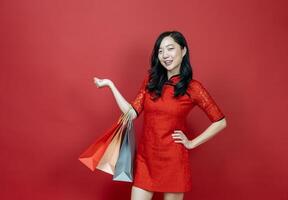 mulher chinesa asiática com cheongsam vermelho ou qipao segurando sacola de compras deseja boa sorte, venda e prosperidade no feriado de celebração do ano novo chinês isolado em fundo vermelho foto