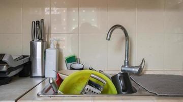 os utensílios de cozinha no lavatório precisam ser lavados. uma pilha de pratos sujos na pia da cozinha. utensílios de cozinha precisam de ser lavados. conceito de lição de casa. foto