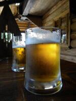 dois Cerveja óculos em a velho de madeira mesa dentro país chalé foto