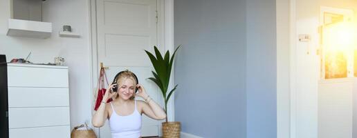 retrato do jovem mulher às lar, conecta para conectados Academia Treinamento sessão, Segue ginástica instruções em computador portátil, vestindo sem fio fones de ouvido durante exercite-se foto