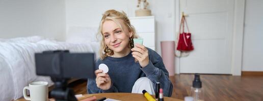 retrato do jovem mulher promovendo beleza produtos, aplica-se Maquiagem dentro frente do Câmera, gravação para dela vlog, criando conteúdo para social meios de comunicação, sentado dentro uma quarto em chão foto