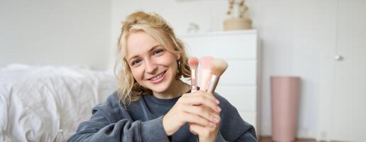 fechar acima retrato do fofa adolescente menina mostrando dela beleza Maquiagem escovas, sorridente e olhando às Câmera foto