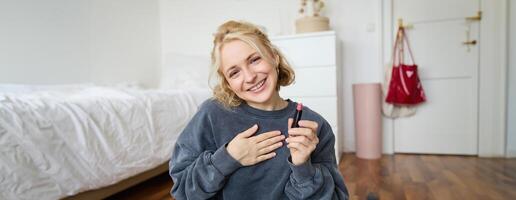 retrato do bonitinho, carismático beleza blogueiro, mulher senta dentro uma quarto com batom dentro mão, falando sobre inventar, conversando com seguidores, gravação conectados corrente em social meios de comunicação aplicativo foto