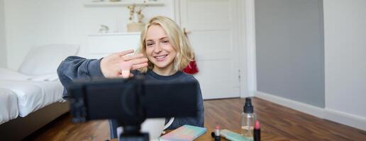 fechar acima retrato do feliz jovem beleza blogueiro, registros estilo de vida vlog dentro dela sala, usando Câmera com estabilizador, mostra Maquiagem escova e cosméticos foto